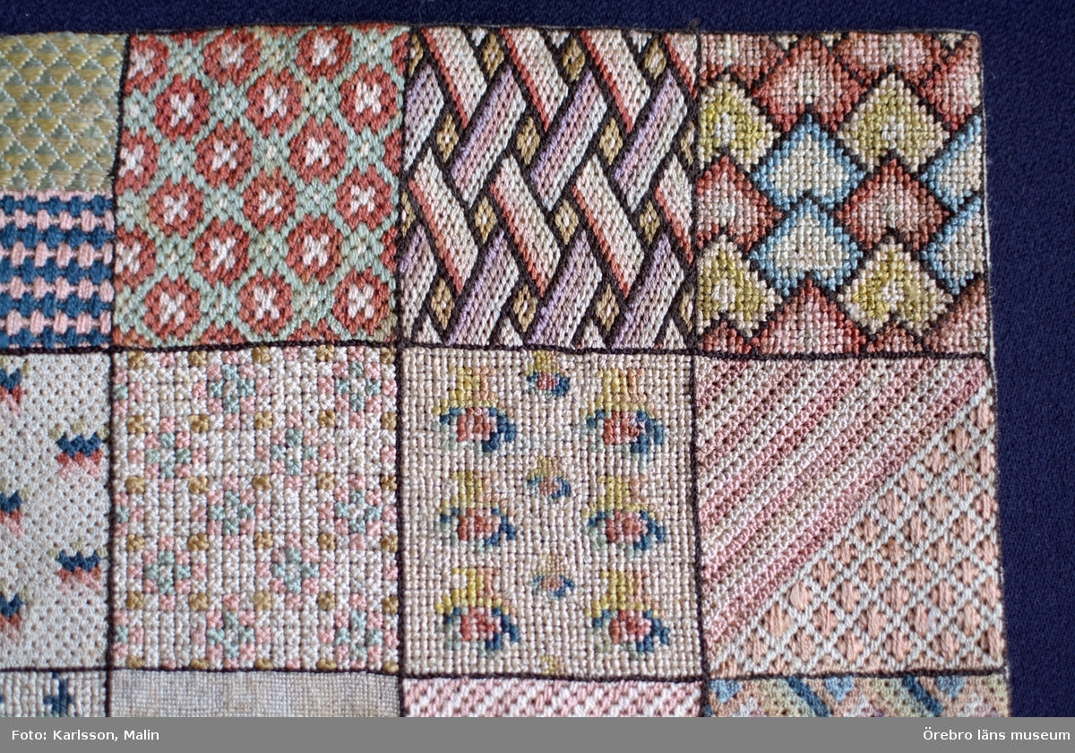 Broderad märkduk bestående av 36 kvadrater med olika mönster.