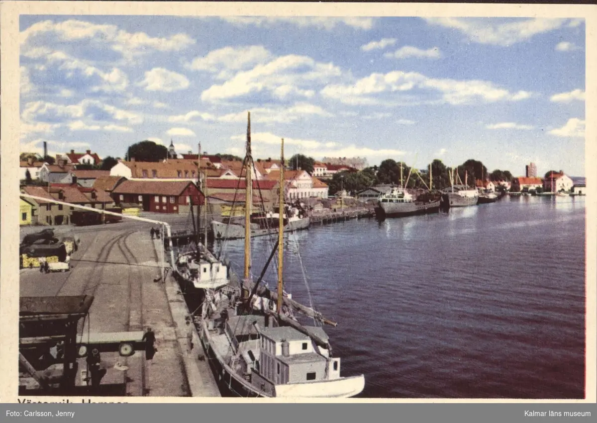 Hamnen i Västervik. Hamnen med järnvägsspår, fartyg utmed kajen. I bakgrunden staden utmed vattnet.