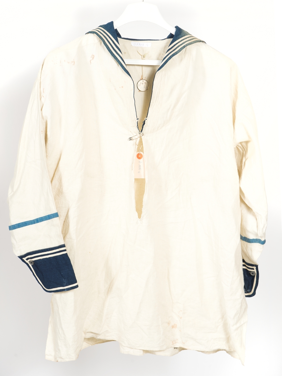 Blåkragad lärftesskjorta med blå ärmuppslag. Tre vita ränder på kragen samt två på uppslagen. Blått redgarnsband på ärmarna samt på den vänstra ankare och tre uppmuntringsvinklar av blått kläde.
Beklädnad till matros 1873.