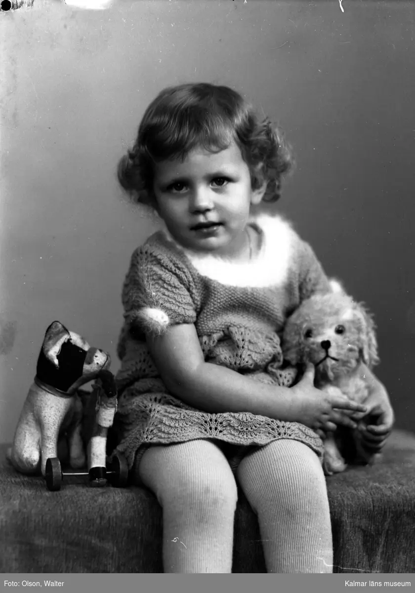 Ateljébild på en flicka med leksaksdjur. Enligt Walter Olsons journal är bilden beställd av fru Alice Johansson.