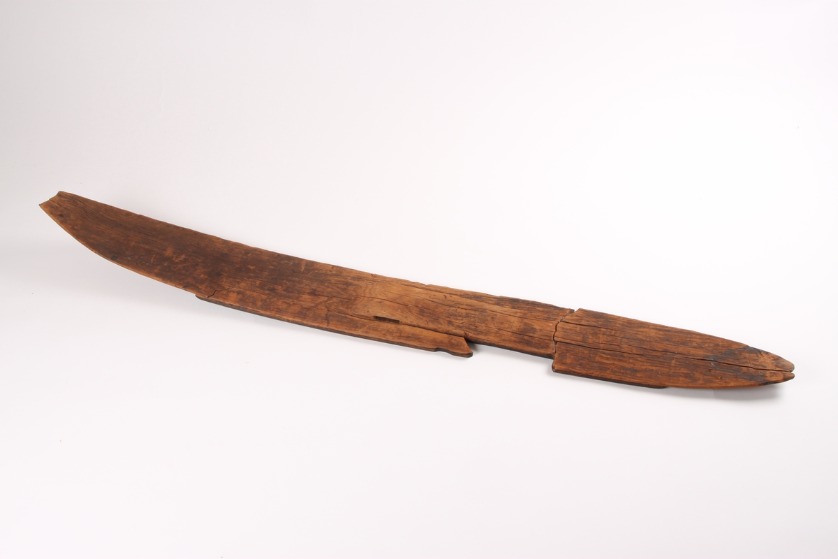 En ski med en lett krummet form og spiss i begge ender. Omtrent midt på skien er det en opphøyning i treet hvor det går et horisontalt hull gjennom skien til å feste bindingen i. På hver side av fotstegplaten og bindingsfestet går det en bred kant. Oversiden av skien er flat, med en noe buet overflate på den ene siden av skien. På undersiden av skien er det påmontert en treplate formet etter skien. Platen er festet med skruer. Skien har to grunne styrerender.