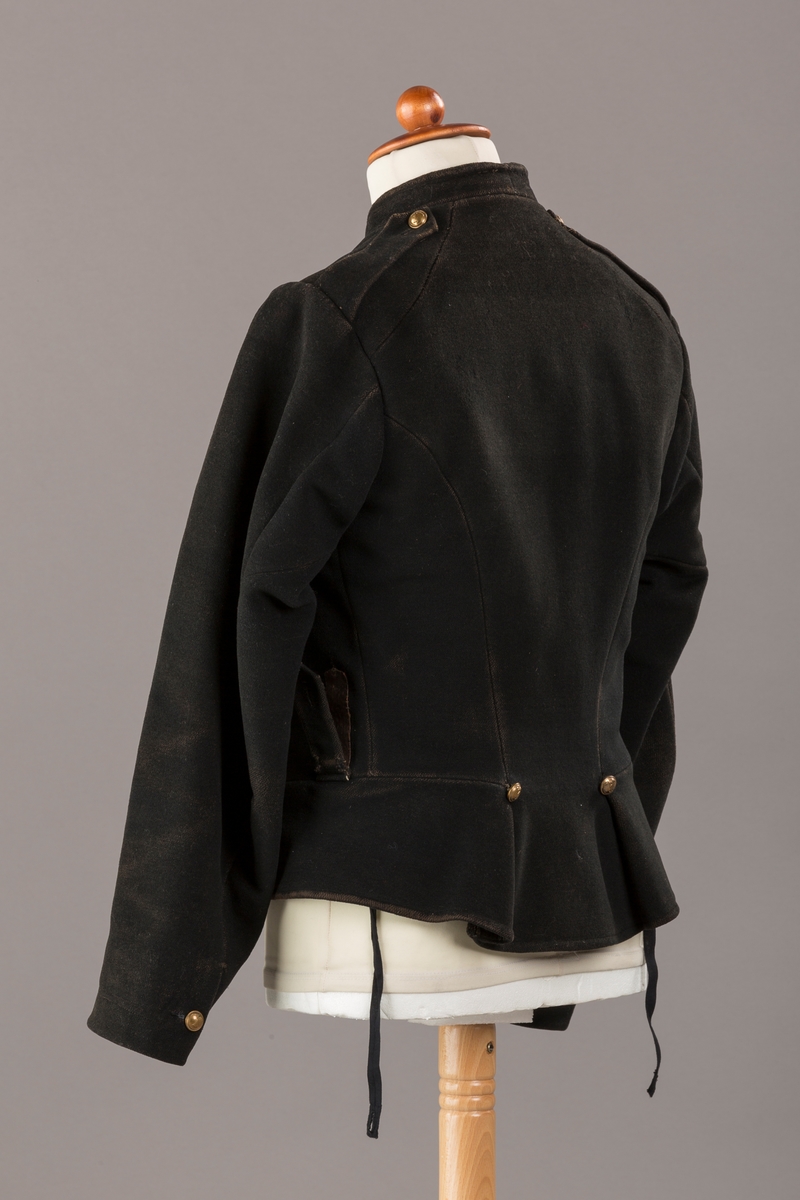 Form: Enkeltspent.

Foret med lin. Forsterket med silke på et lite stykke på ryggen. 12 messingknapper med mønster og tallet 1. Hempe i lin. Bendelbånd med knappehull.