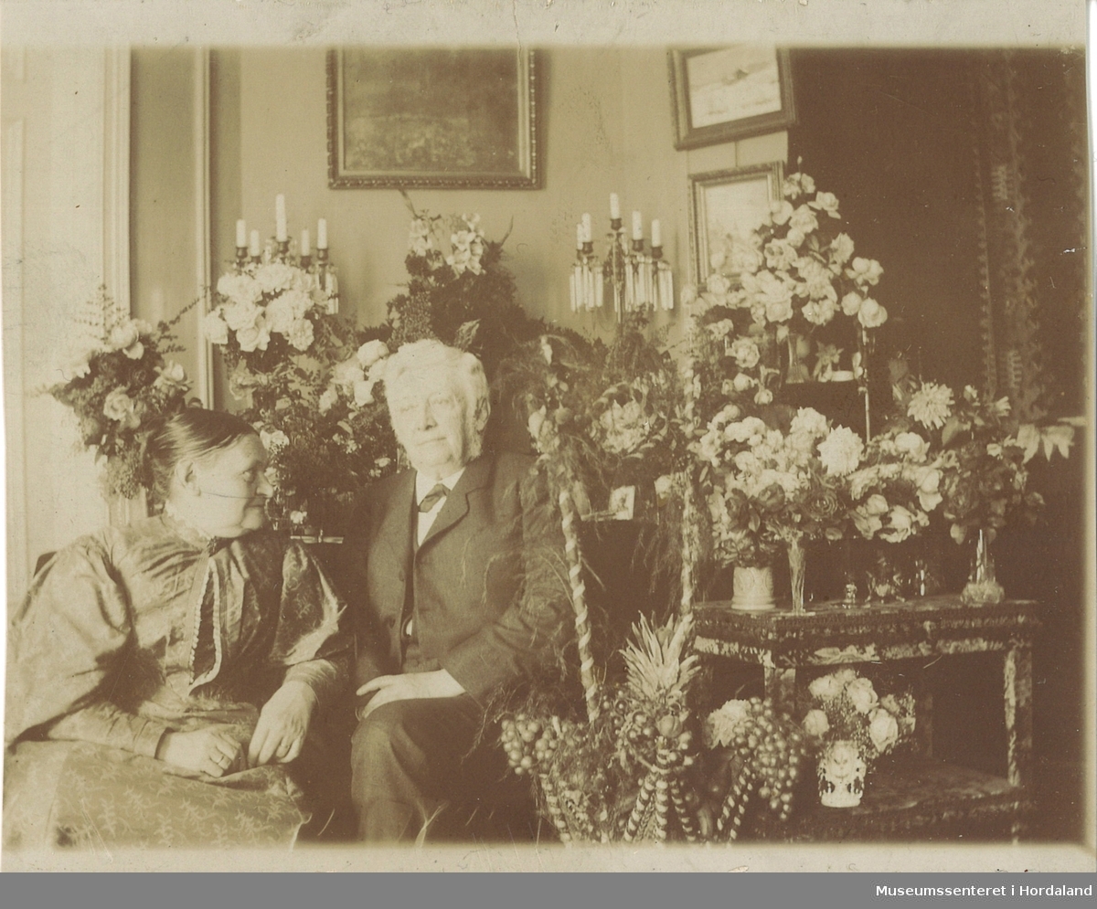 amatørfotografi av eldre mann og kvinne som sit framfor eit bord fullt av blomster