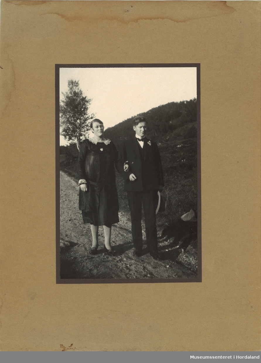 amatørfotografi av kvinne og  mann i mørke festkle som står på ein grusveg med grasbakke og ei enkel bjørk i bakkanten 