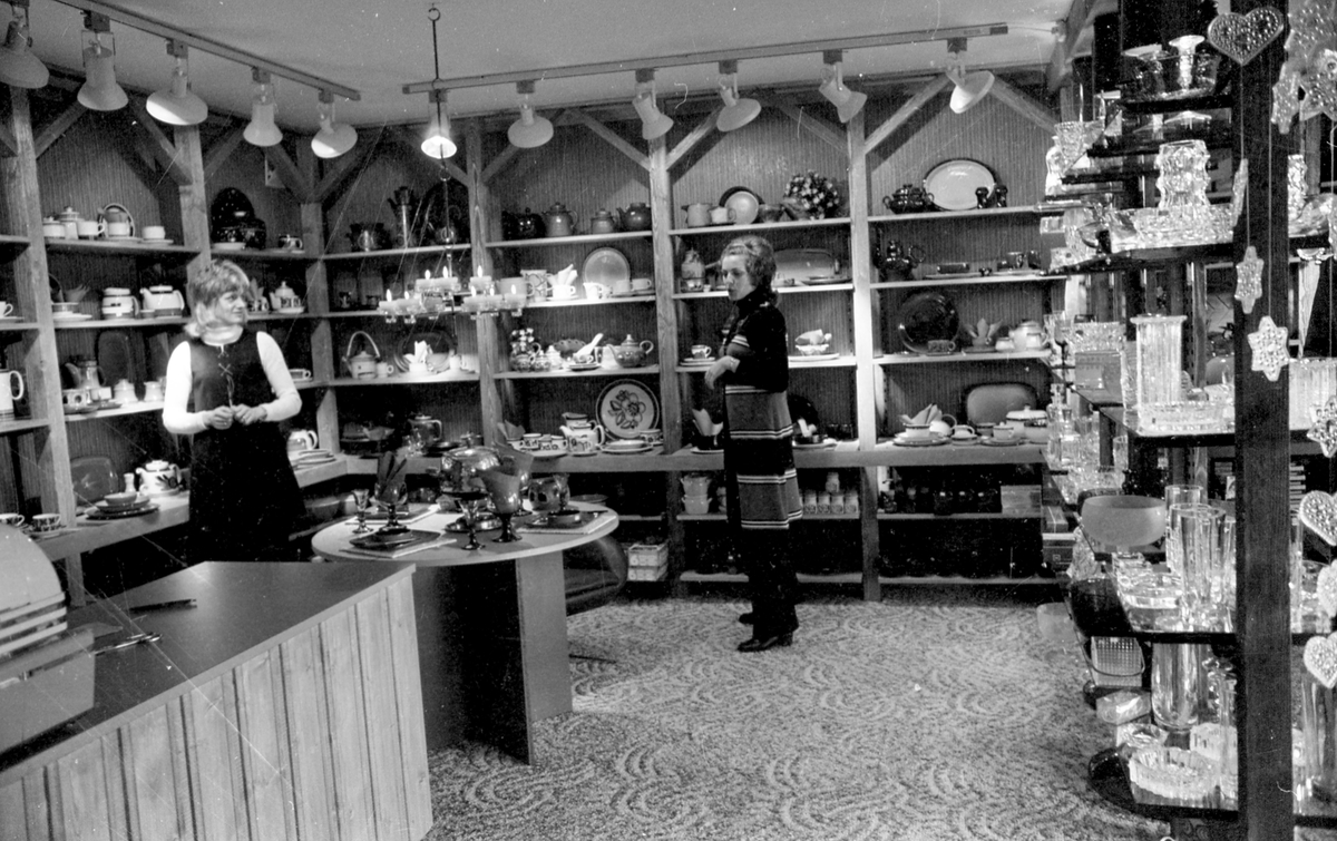 Interiør i en gavebutikk som selger glassvarer og pyntegjenstander. Hyller med varer på utstilling. Ekspeditører og  kjøpelystne kunder.