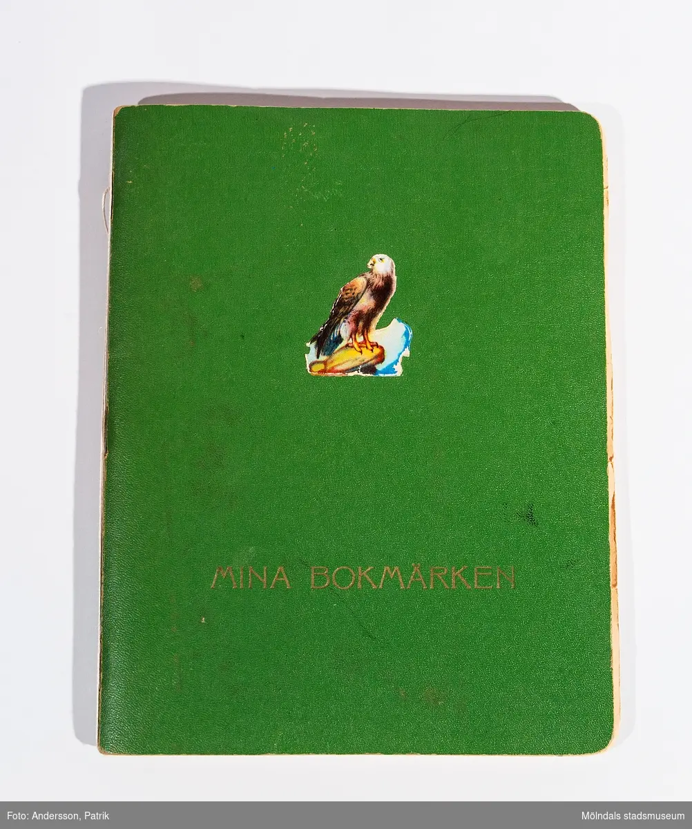 Bokmärkesbok med inklistrade, tidstypiska bokmärken. På framsidan står tryckt: MINA BOKMÄRKEN. Ett bokmärke, föreställande en örn, är klistrat ca 10 cm ovanför texten. Boken ägdes/användes av givarens mor Ninnie Johansson.
