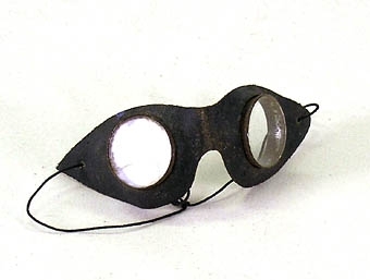 Skyddsglasögon av läder och oslipat glas. Resårband för att fästa runt huvudet.