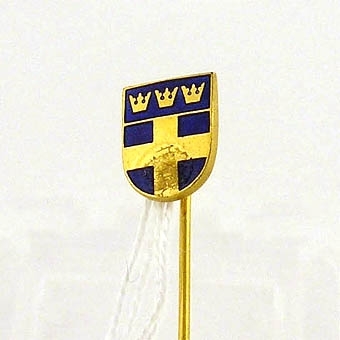 Nål med huvud i form av en enkel sköld, tre kronor och svenska flaggan.

Enligt liggaren: Förenings- och idrottsmärken, 25 st. uppsatta på en tygremsa.