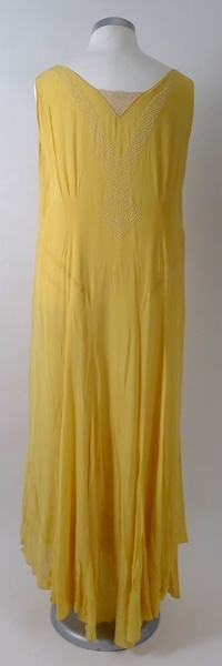 Lång sidenklänning av gul georgette, broderad med vita pärlor. Spets i urringningen både fram- och baktill på klänningen. Underklänning av gul crepé  de chine.