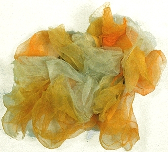 Klänningsdekoration av tunt silke i vitt och gula nyanser, hoprynkat till en blomma och uppsytt på svart, styv tygbit, rund. Handsytt.
