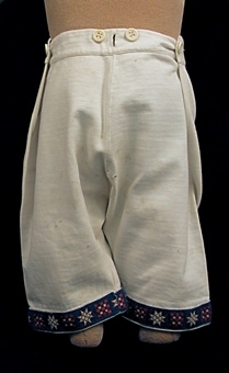 Kostym bestående av två delar, tröja och knäkort byxa. Kostymen är sydd av oblekt bomullstrikå. Runt halsringningen, ärmarnas- och benens nedre kant  är ett mönstervävt band fastsytt. Bandet har en mörkt blå botten med geometriska mönsterfigurer i färgerna grönt och rött. Tröjan har en rakt skuren bål, isydd kort ärm samt knäppning på vänster axel med två vita metallknappar. Byxan har sprund i sidorna. Linning av kypertvävt bomullstyg. I linningen är sex knappar för hängslen fästa. Lodrätt knapphål i linninKost


Neg.nr: 
Sakord: KOSTYM
Tillverkningstid: 1915 - 1920
Material: Bomull
Teknik: Stickat vävt sytt
Mått: L=överdeL=485  L=byxa 400
Vikt: