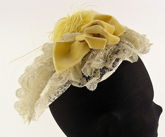 Hårklädsel av vit tyllspets, gula sammetsband och fjäder.

Neg nr 1985-09