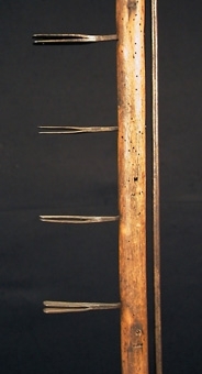 Enl liggare:
"Ljuskärring (?) Trästång med rund fot, två träskivor trädda på stången och mellan dessa en svarvad träskål. På övre delen av stången fem klämmor av järn, möjligen till att fästa trästickor i. En smal järnten utmed övre hälften - okänd användning H 114 cm, br 25 cm. Defekt."