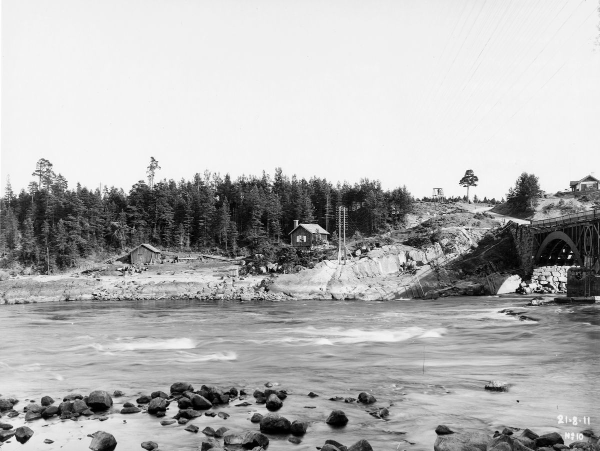 Kraftverksbygge. Den 21 augusti 1911. Älvkarleby kraftverk är ett vattenkraftverk i Älvkarleby, cirka 8 km från Dalälvens mynning. Det byggdes av Vattenfallsstyrelsen nuvarande Vattenfall AB och togs i drift 1915. Carl den XIII:s bro, Café "Neptun".