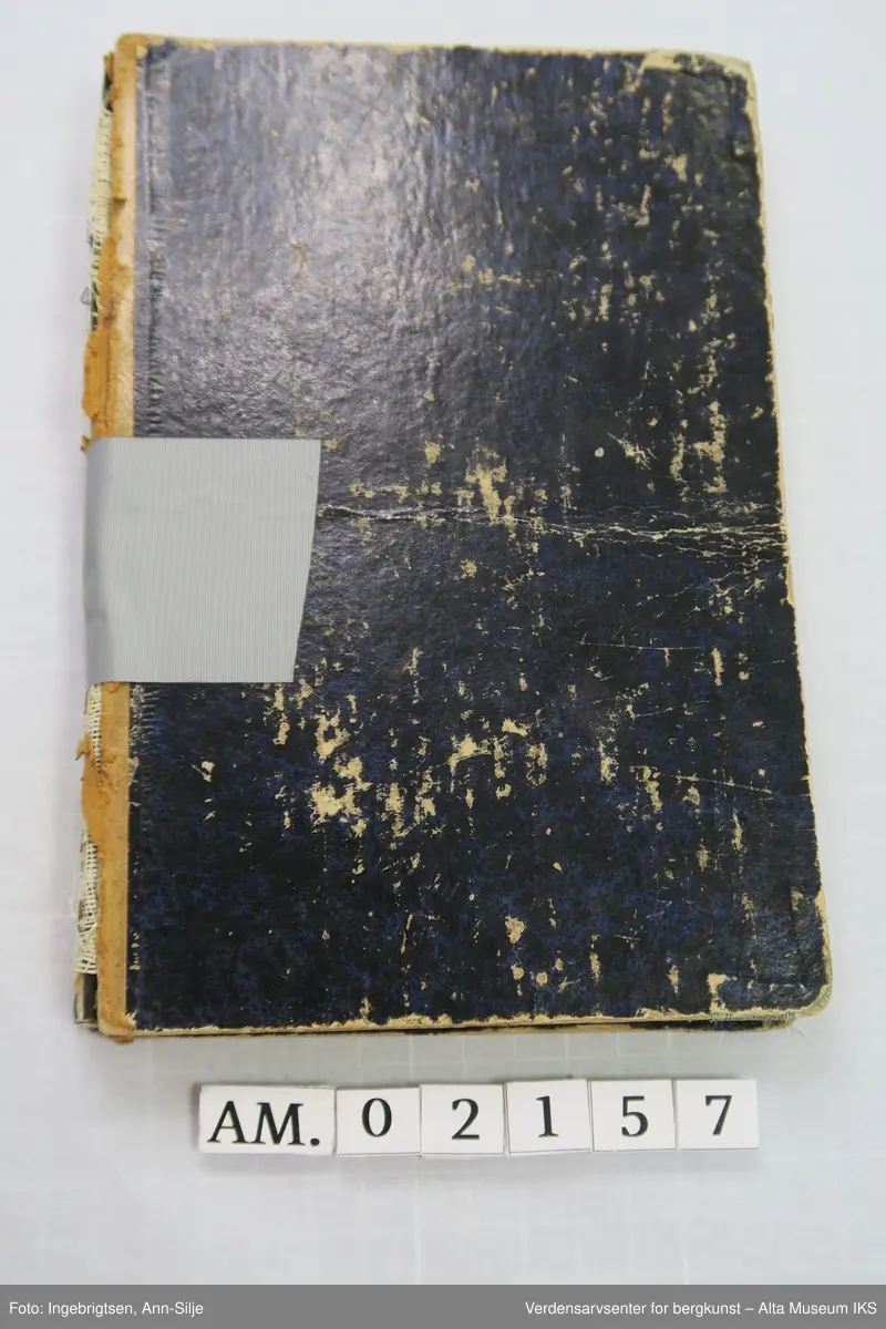 Bok med svarte permer. Ryggen på permen er ødelagt og permene blir holdt sammen av en grå tape.