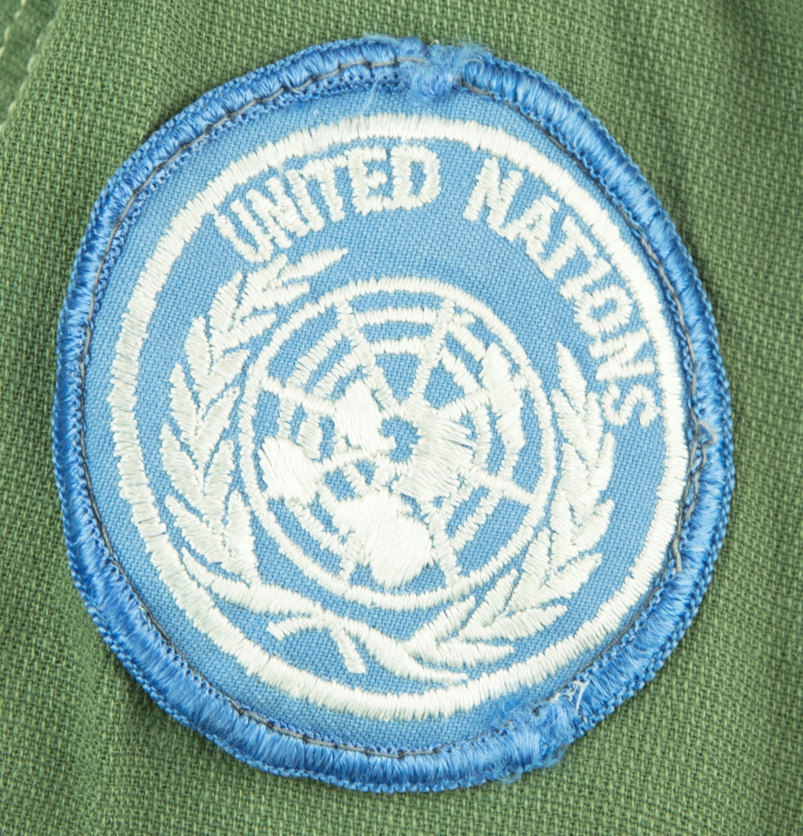 Skjorta i ljus militärgrön, brukad vid FN-tjänst. Två bröstfickor fram med knäppning. Knäppning fram med fyra knappar. Slejf på vardera axel för axelklaffhylsor. På vänster axel (framifrån) sitter ett ljusblått tygmärke med FN logga, på höger axel sitter ett tygmärke med Svensk vapensköld och texten "SWEDEN" i gult. Storlek XL.