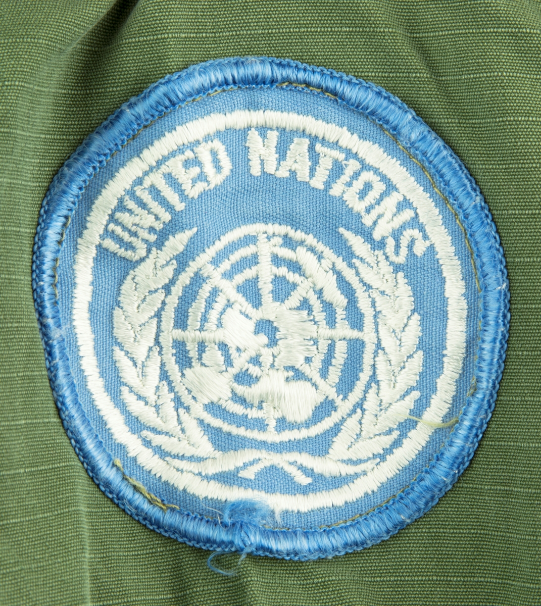Vapenrock av modell m/61.  Vapenrocken är militärgrön och brukad vid FN-tjänst. Två bröstfickor fram med dold knäppning. Dold knäppning fram med synlig övre knapp vid halsringning. Slejf på vardera axel för axelklaffhylsor. På vänster axel (framifrån) sitter ett ljusblått tygmärke med FN logga, på höger axel sitter ett tygmärke med Svensk vapensköld och texten "SWEDEN" i gult. Storlek Medium/Regular.