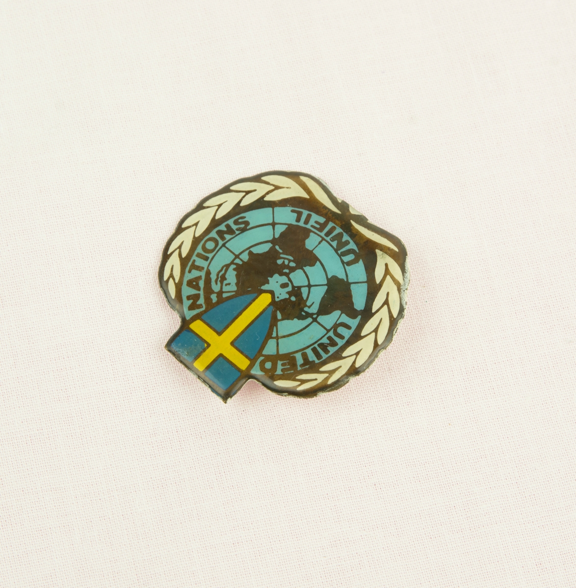En pin från utlandstjänstgöring med motiv av FN loggan med en sköld med svenska flagga i mitten. I texten står "UNITED NATIONS UNIFIL". Fästes på kläderna med nål på baksidan.