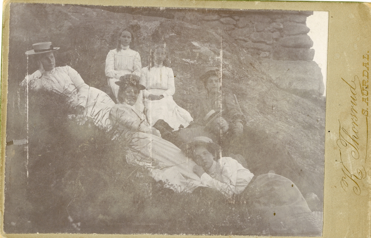 6 kvinner/jenter ligger i graset foran en steinmur.