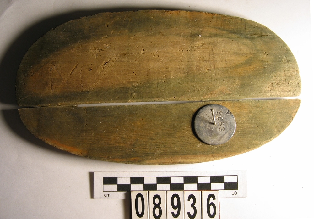 En oval botten till en svepask. Bottnen är i två delar. På bottnen finns spår efter åtta träpligg. På undersidan finns ett inristat M.