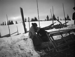 Fjellandskap, kvinne sitter ved skigard, ski, slede