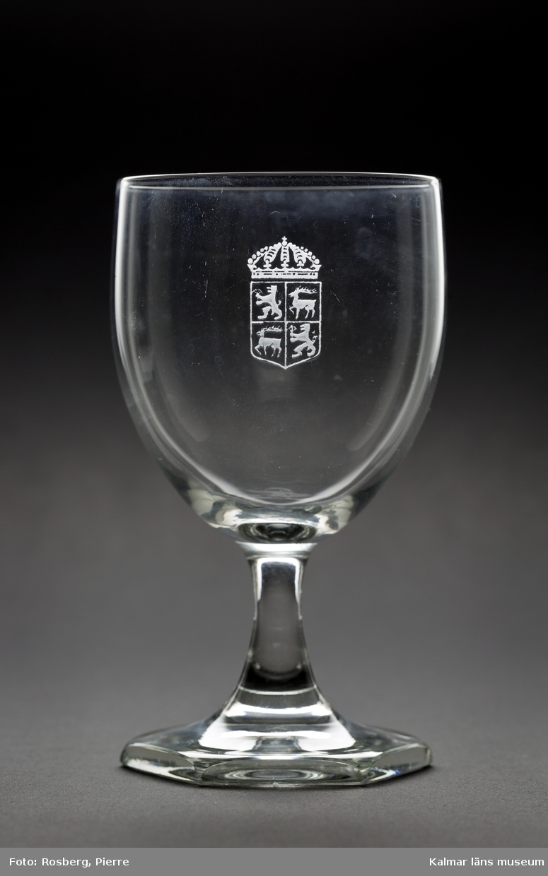 KLM 44717:15 Rödvinsglas, av glas. Glaset är tillverkat av Orrefors glasbruk och kupan är graverad med länsvapnet. Liten flisa saknas på fotens undersida.