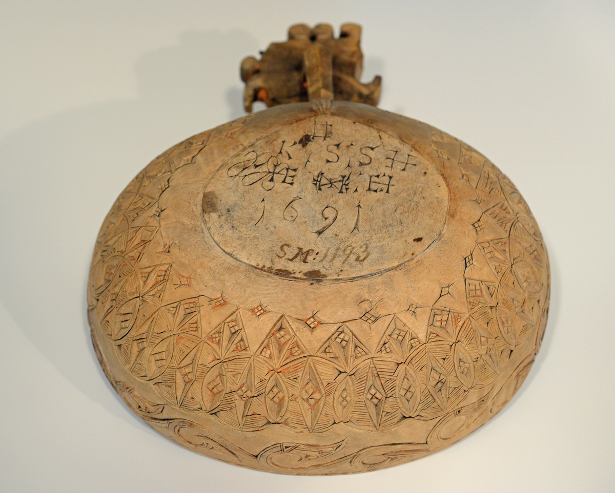 Oval øløse i tre med bredt skaft. Øløsen er dekorert med treutskjæringer i to border på korpus , samt utskjæringer på skaftet. Skaftet mangler en del av dekoren. Det er spor etter tidligere rødmaling.