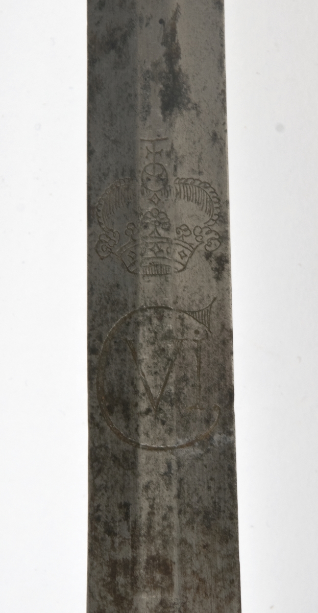 Dansk/Norsk Soldatkårde modell 1701. Plommeformet knapp merket N 55.. Tregrep med messingtråde bevikling og hylse oppe og nede. Nyreformet parerplate med 9 fliker. Nedbøyd bakre parerstang. Fremre parerstang går over i håndbøylen og er tappet i knappen.
Rett tveegget klinge med 6 kantet tverrsnitt. Klingen er merket med kronet Christan 6 monogram som C VI