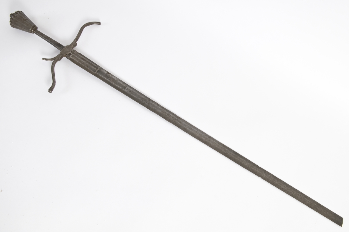 Vaseformet knapp som er fasetert og med skulpturert topp, samt nitteknapp.  
Grep mangler.
S-formede parerstenger, resten av grepet mangler.
Klingen har 6-kantet tverrsnitt med 3 korte blodrender og avbrukket spiss.
På begge sider av klingen løpende ulv, pluss innskripsjon: WHIM og KLEIH.
Innskripsjoner og ulver er innlagt med kobber.