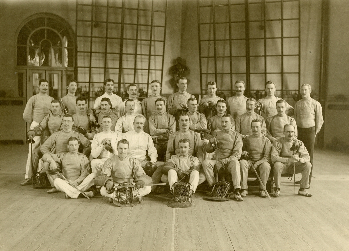 Grupporträtt av fäktare i gymnastiksal, omkring 1900.