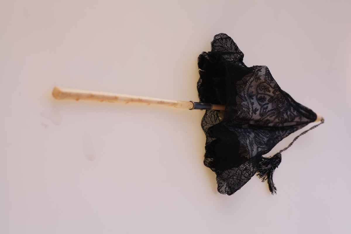 Parasoll av hvit silke og svart blonde over en stav av elfenben.