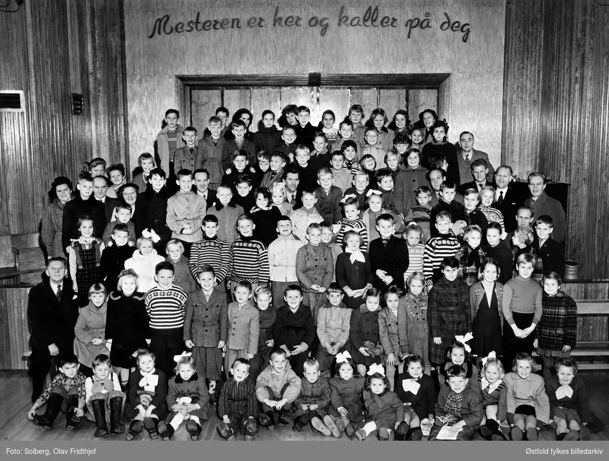 Søndagsskolen på Betania i Kirkegata, Sarpsborg ca. 1953-54. Alle barn, hjelpere og søndagsskolelærer. Personer ukjent. 
Tekst på veggen: Mesteren er her og kaller på deg.