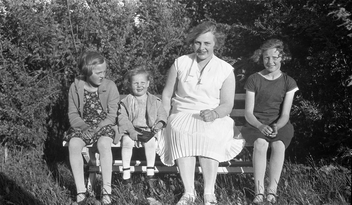 En kvinne og tre jentunger i forskjellig alder i helfigur på en krakk. Ingen av de fire er identifisert.