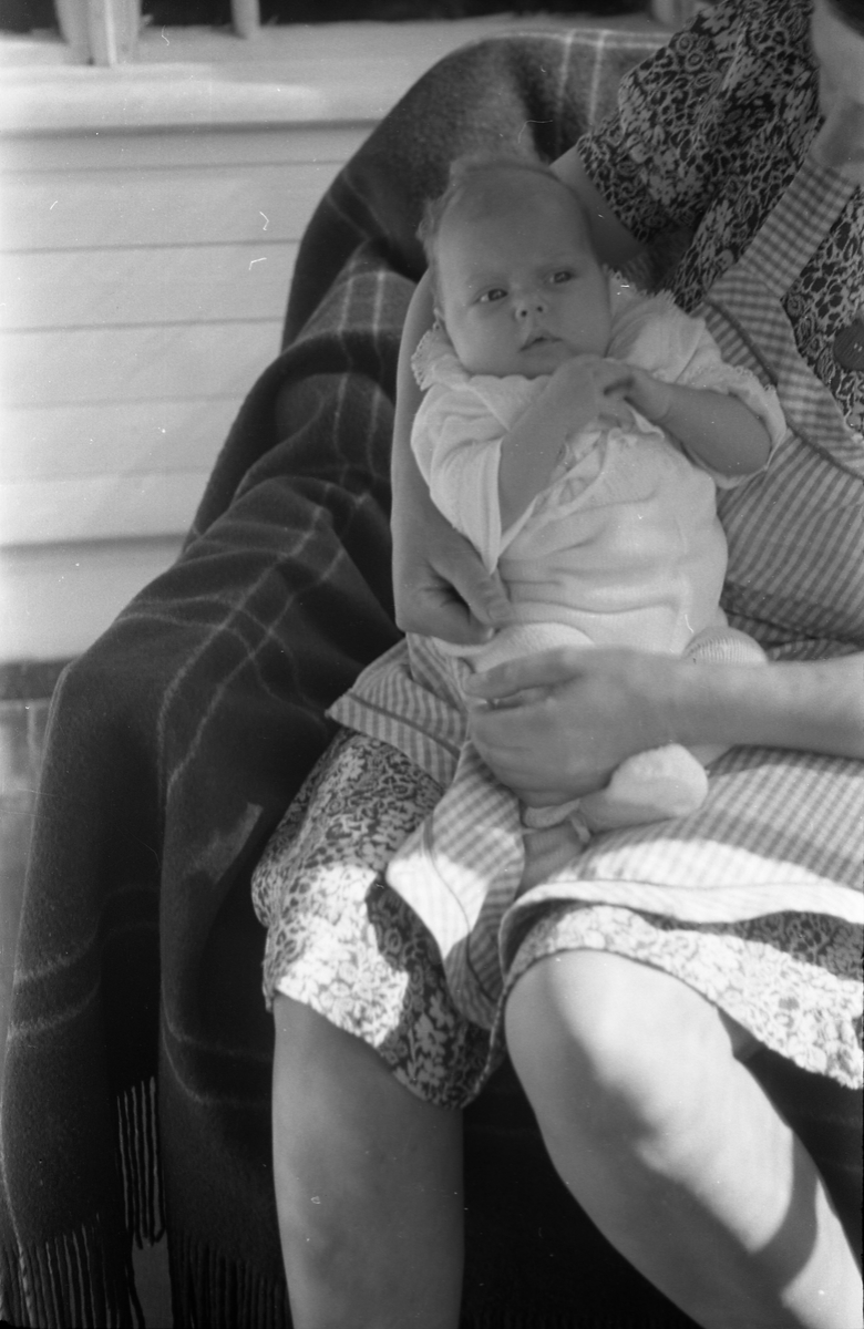 Uidentifisert lite barn. Serie på 10 Bilder. På noen av bildene holdes barnet av kvinner som bare delvis vises, og som heller ikke er identifisert.