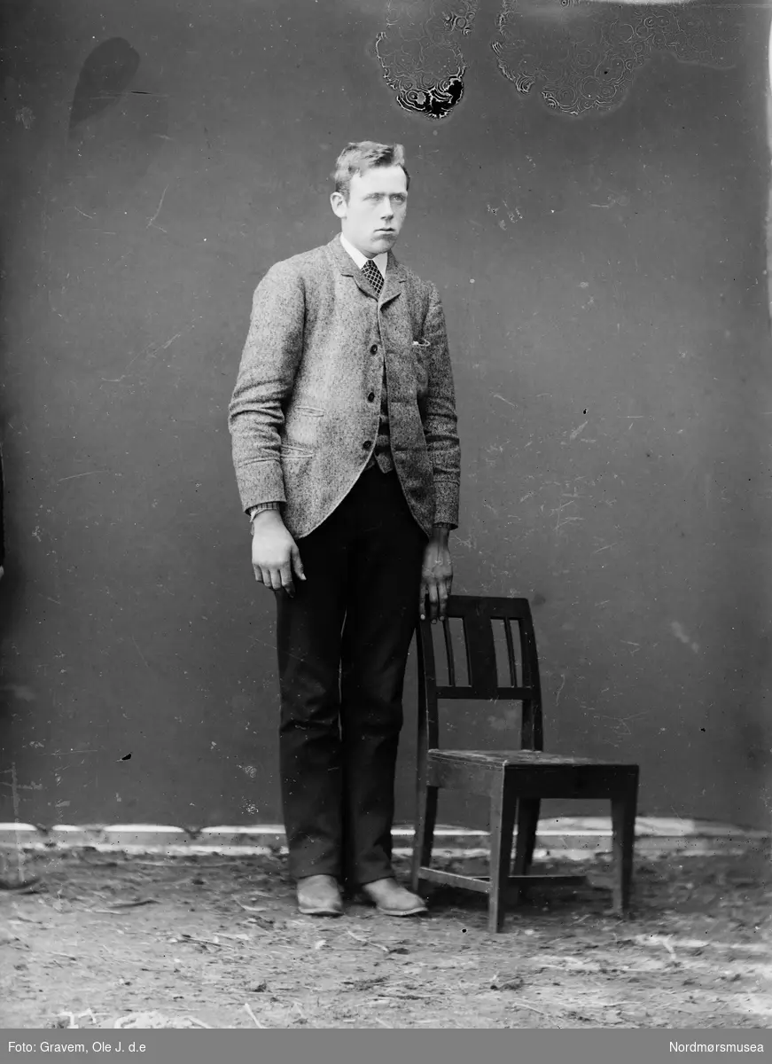 Mann stående i atelier ved en stol. Portrett i helfigur.