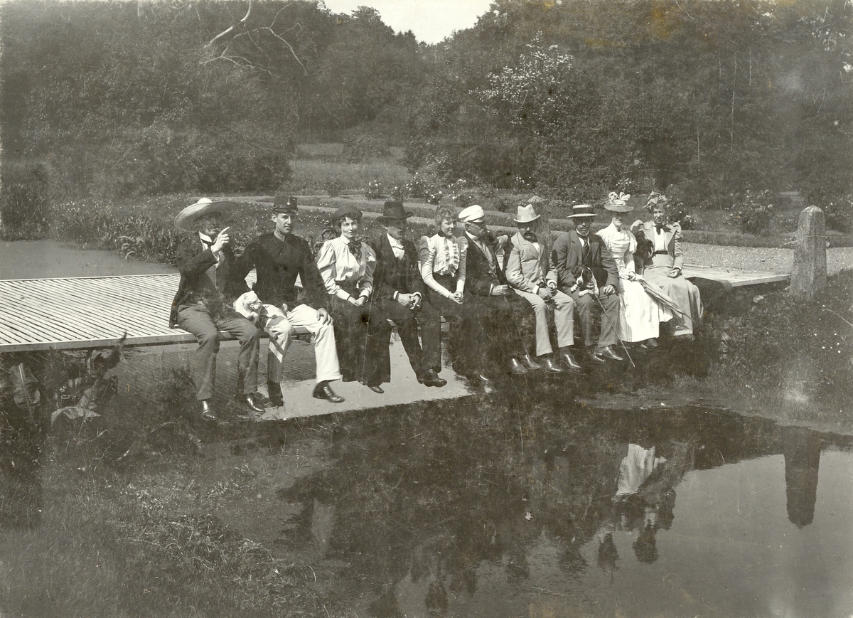 Kvinnor och män sitter på en liten träbro, sommaren 1898.
För namn, se bild nr. 3.