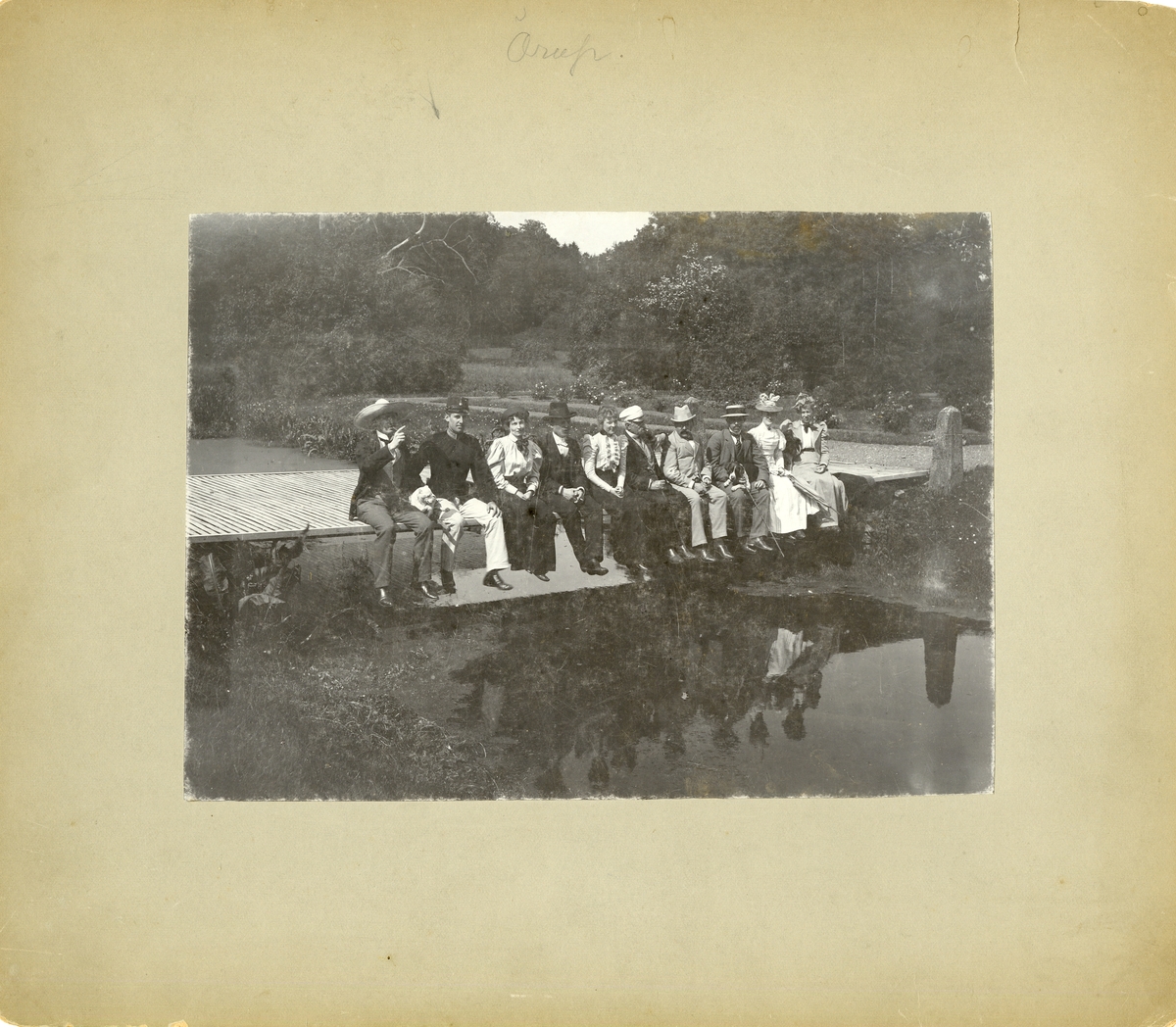 Kvinnor och män sitter på en liten träbro, sommaren 1898.
För namn, se bild nr. 3.