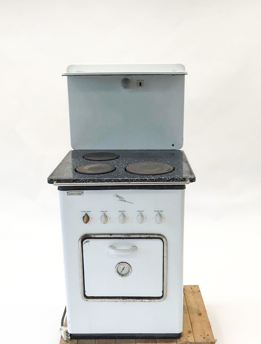 Elektrisk komfyr med bakvegg og tre kokeplater. Stekeovn med termometer på utsiden. I stekeovnen er det to tilhørende stekebrett. Lyspære på bakveggen.
