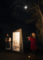 Munk i hvitt og svart synger mens mann i rød middelalderjakke og struthette spiller fiolin. Over lyser månen fra den mørke høsthimmelen. (Foto/Photo)