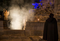En mørk skikkelse i kappe ser fram mot en hvit engel som står i lys og røyk. (Foto/Photo)