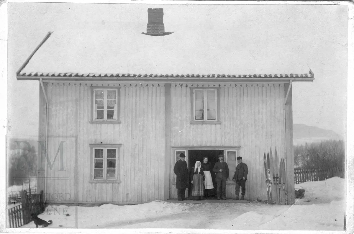 Prestkvern gård ca 1900. Familie, fem personer står ved inngangen til huset. 3 par ski står opp etter veggen.