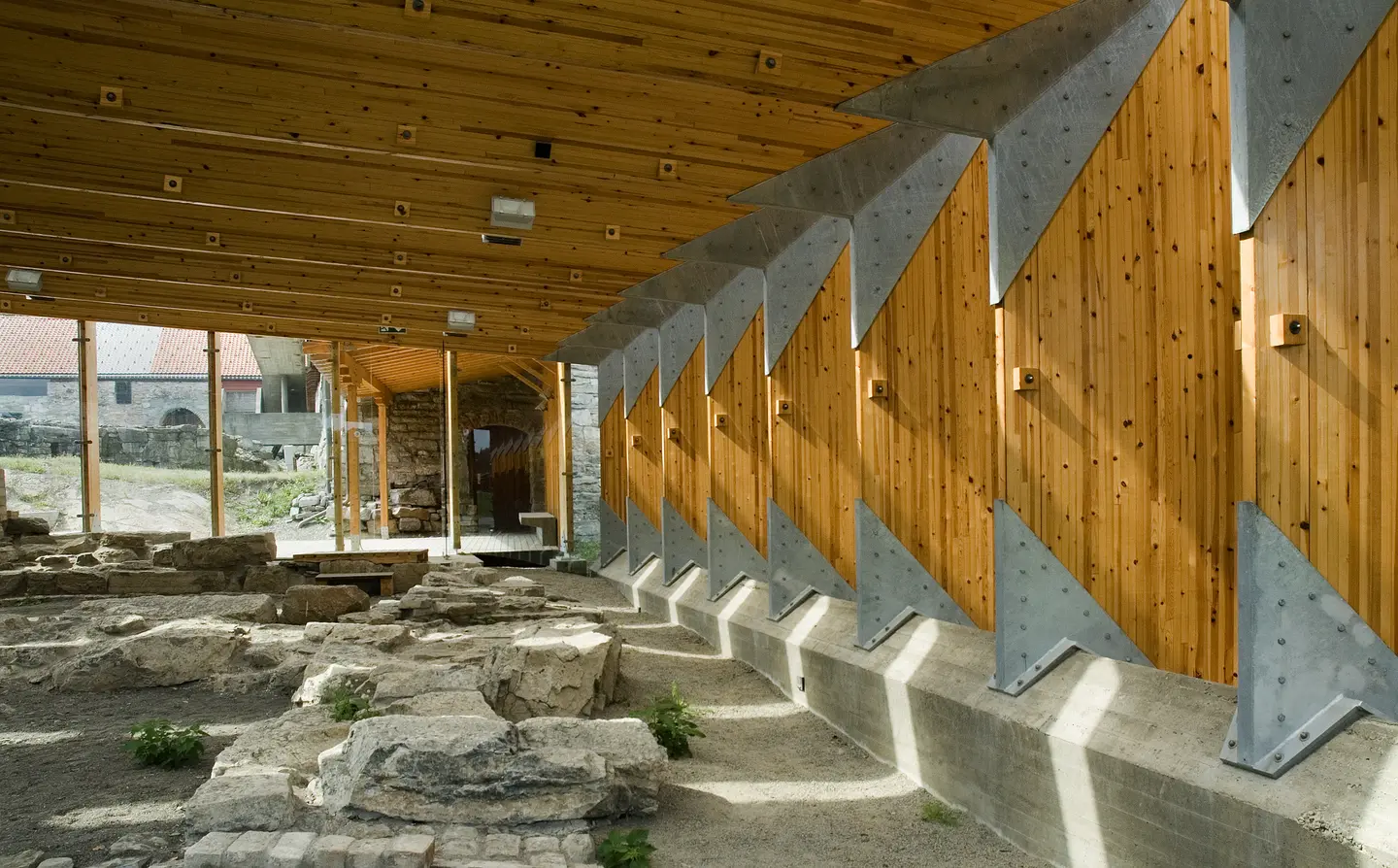 Vernebygg av Sverre Fehn, over middelalderruin: Trehvite limtrebjelker i trekantfasong står festet til betongkant med solide, trekantede metallbeslag. Limtrebjelker i taket hviler på de stående og er festet med trekantede metallbeslag. I endeveggene og mellom limtrebjelkene er det glassfelter som slipper inn mykt lys.