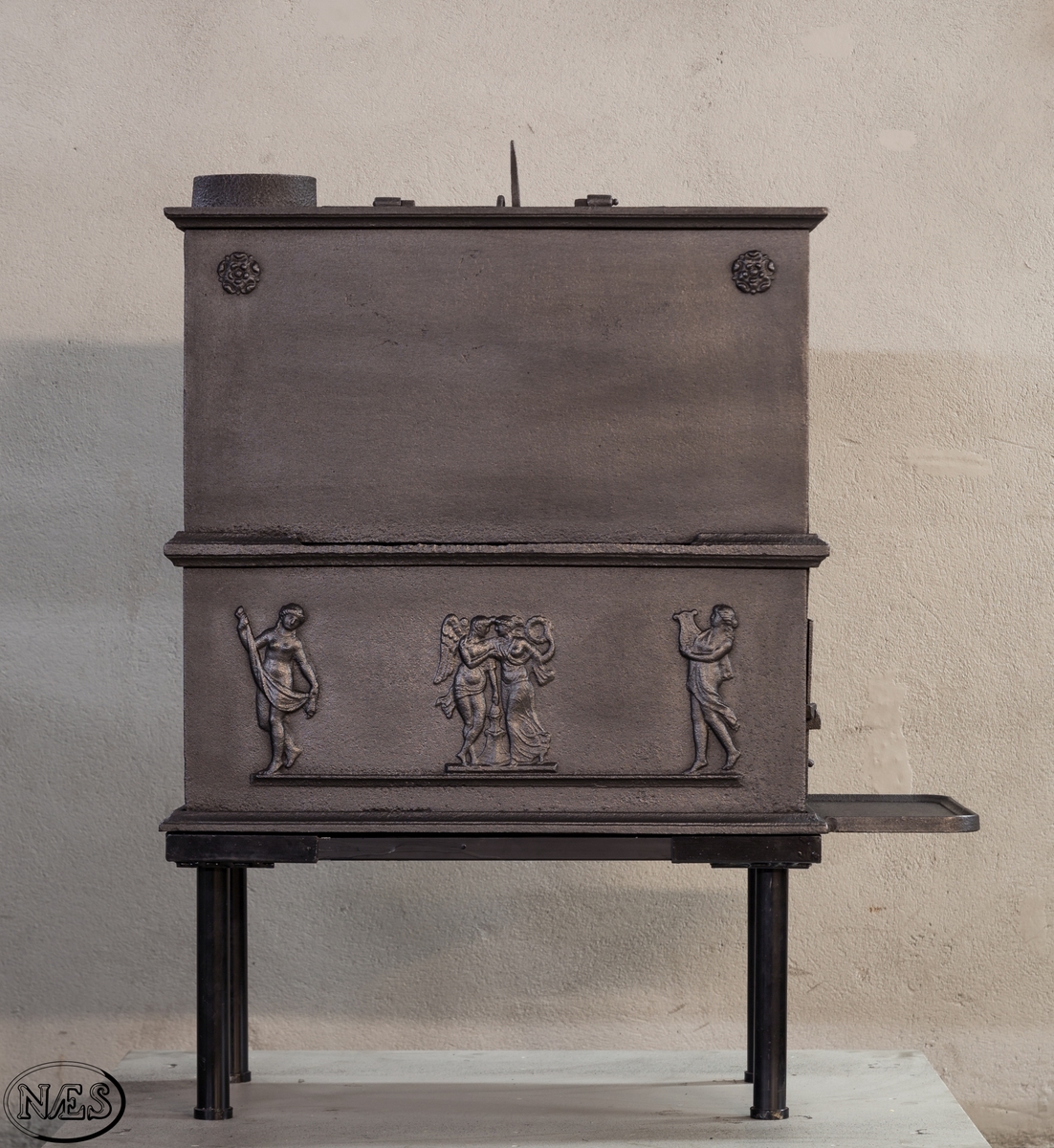 Kokeovn i to etasjer med eget fyrkammer og kokerom. Kokerommet kan åpnes med to dører på langsiden og med en luke i topplaten. Ovnsdøren til fyrkammeret er på kortsiden 1 etg. På langsidene i 1. etg er det tre muser og en engel med lette draperier på en enkel profillist. På kortsidene 2. etg er det draperikledd dansende muse på enkel profillist med en rosett i hvert øvre hjørne. Langsidene i 2.etg er dekorert med en rosett i hvert øvre hjørne.