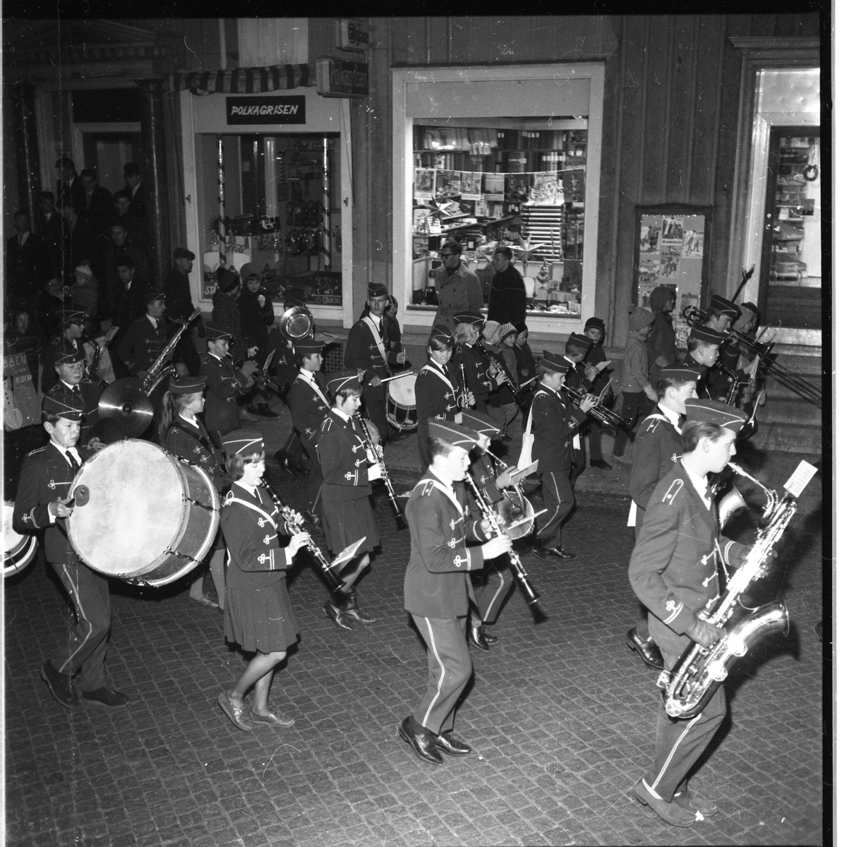 Okänd musikkår marscherar och spelar på Brahegatan i Gränna, passerar bl a Holgers pappershandel, i samband med Lucia 1963.