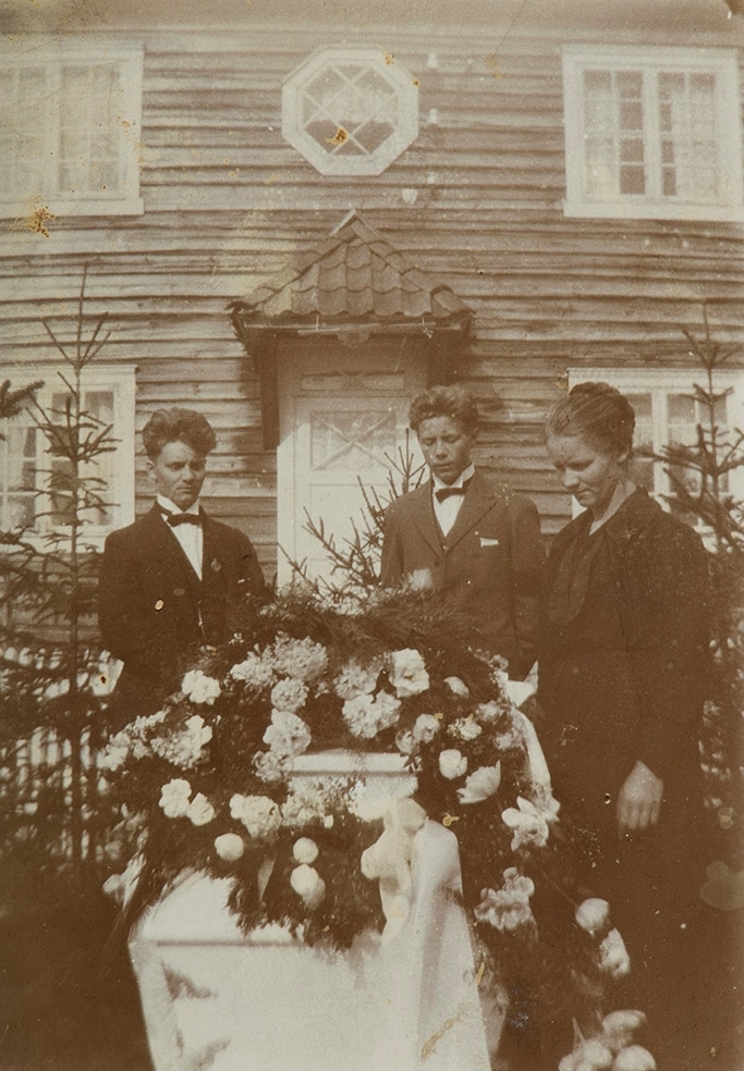 Begravelse, blomsterkranser, Ved kisten, f.v. Rudolf Larsen,  Anders Larsen, ukjent kvinne. Bildet tatt utenfor Skjærdal på Klevfos, Løten.