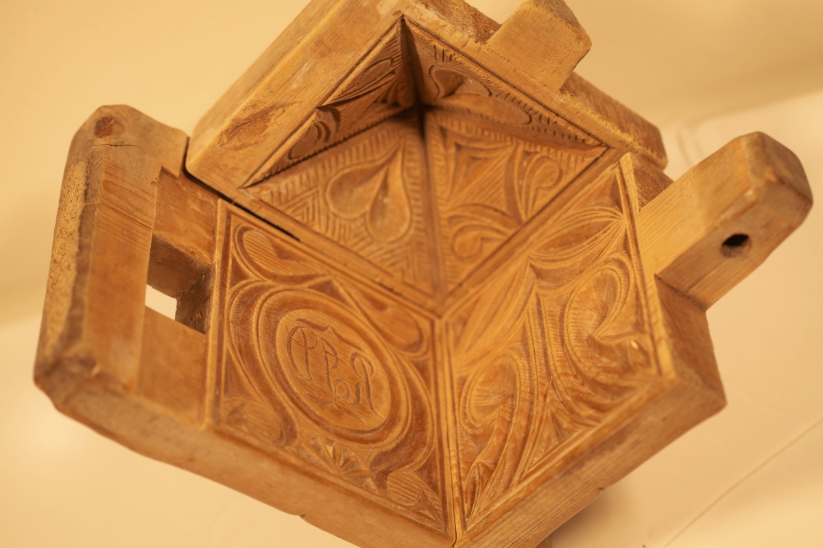 Smørforma er firkanttet med pyramideformet lokk, utskårne hjerte, blad og stjerne.