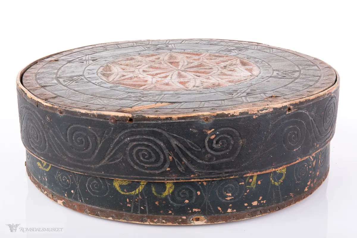 Seksbladsrose i karveskurd sammenkomponert med andre geometriske figurer sentralt på lokket. Dekorfelt rundt midten av lokket med kryss og spetter, N- formet bord o spetter ytterst. Lokktrosken har bølgeformede ranker. Små gjentagende blomsterbuketter på esketrosk. Innrisset passerrose i bunne  innvendig.