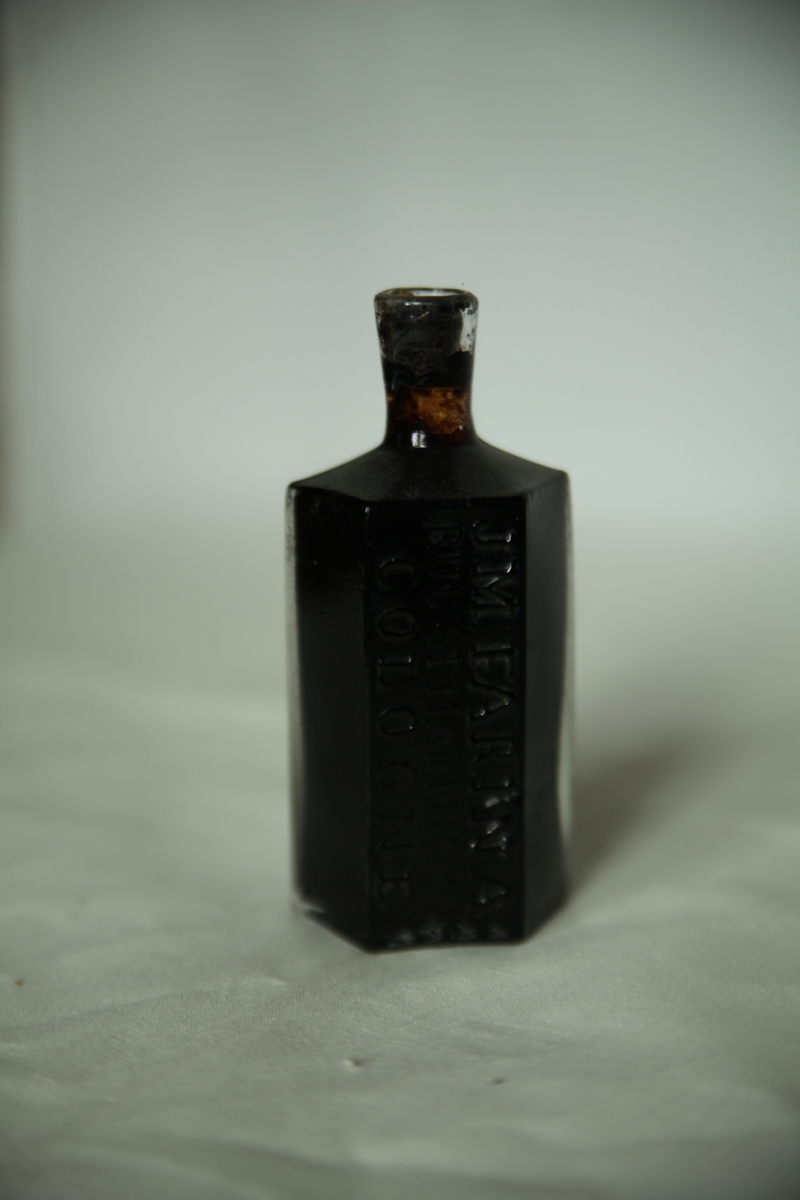 Sekskantet brun Cologneflaske med pontemerke. Korken sitter i. Halsen sitter på forholdsvis rette skuldre.