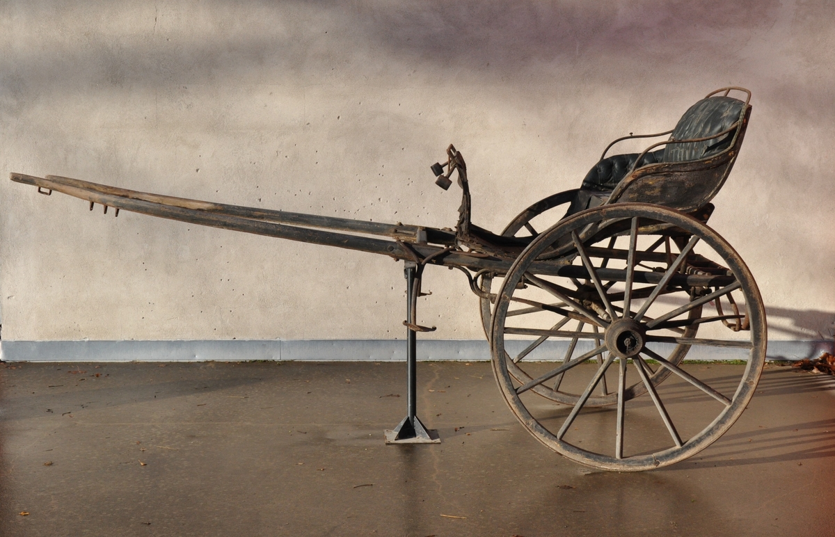 2-hjuls vogn for én hest til persontransport. Sete utført som rammeverk med fyllinger hvilende på jernbeslag.