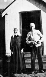 Portrett av eldre ektepar foran bolighus. Tjøstell og Inger 